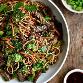 Beef lo Mein with broccoli, snap peas and shredded carrots in a white bowl.