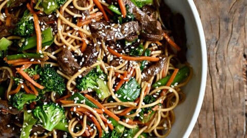 Beef lo Mein with broccoli, snap peas and shredded carrots in a white bowl.