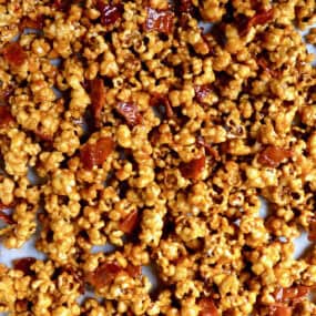 Caramel popcorn with bacon on a parchment-lined baking sheet.