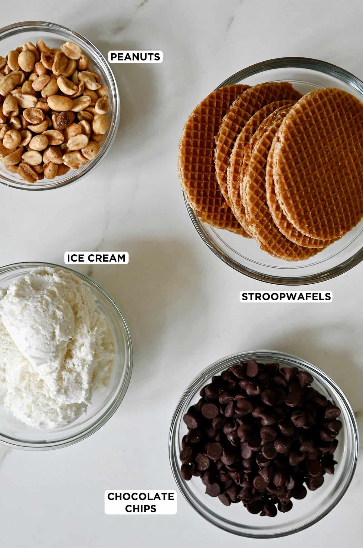 Stikliniai dubenys, kuriuose yra naminių šokoladinių taco ingredientų: žemės riešutų, stroopwafelių, šokolado drožlių ir vanilinių ledų.