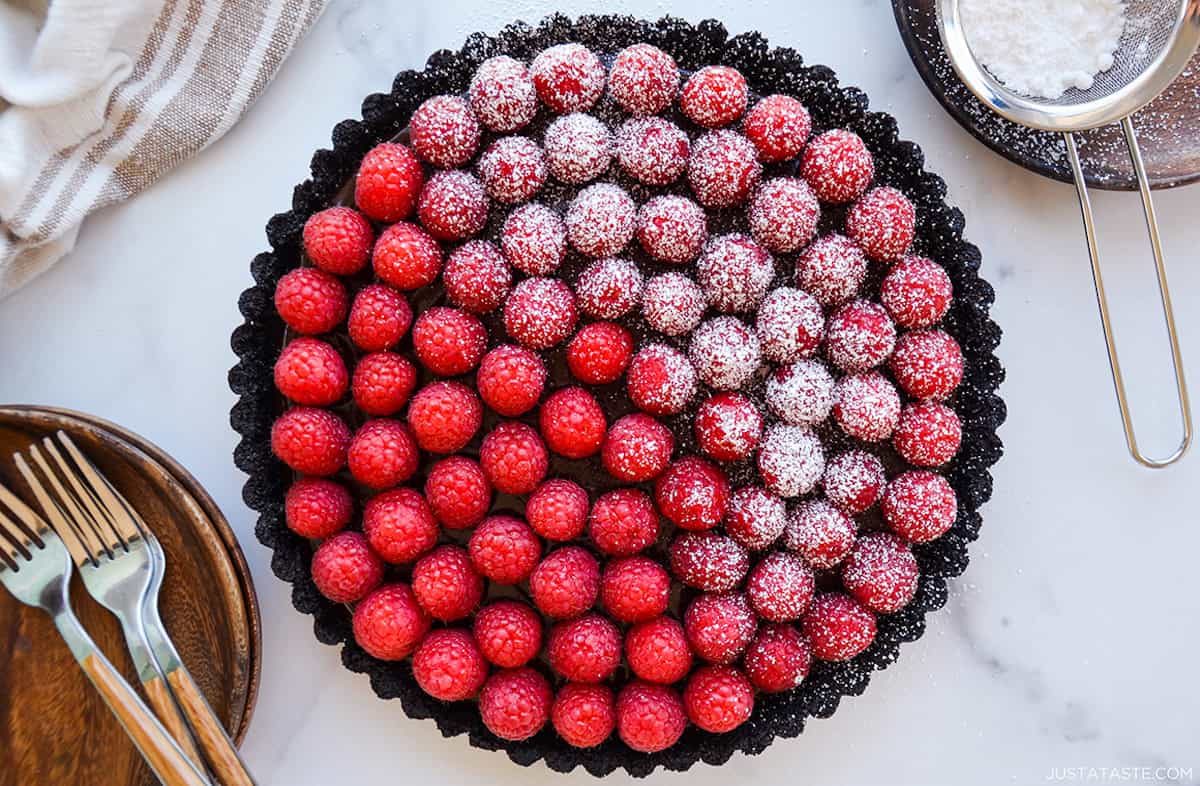 A chocolate tart topped with fresh raspberries. Half of the tart is dusted with powdered sugar.