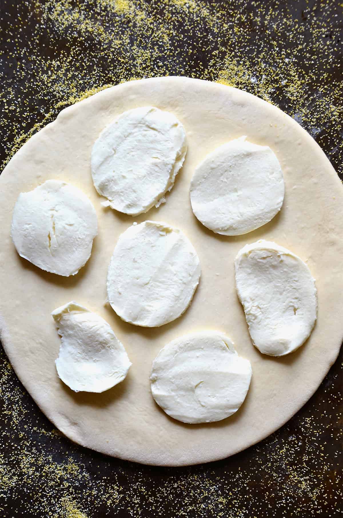 Slices of fresh mozzarella atop pizza dough on a corn flour dusted surface.