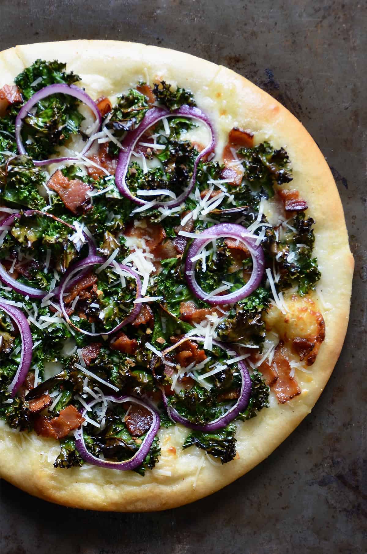 Kale and bacon pizza topped with grated parmesan cheese and red onion slices.