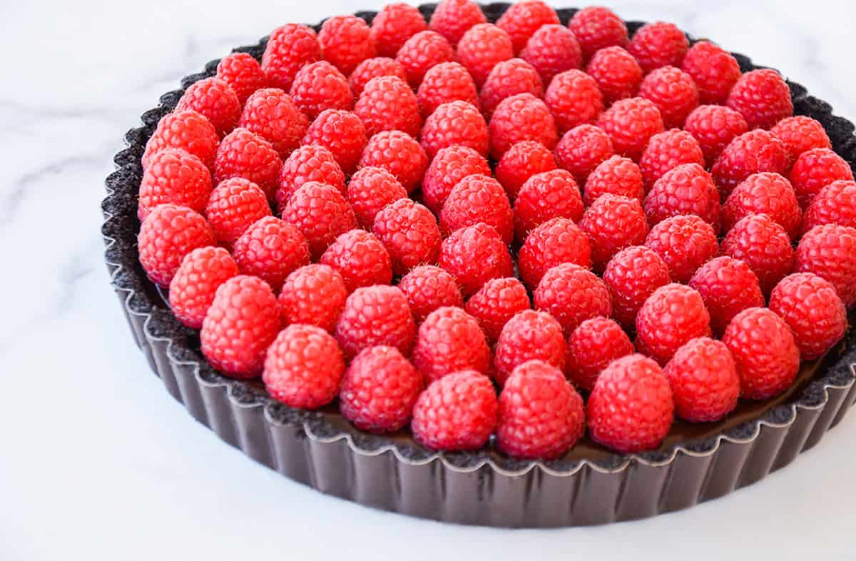 A chocolate tart in a tart pan topped with fresh raspberries.