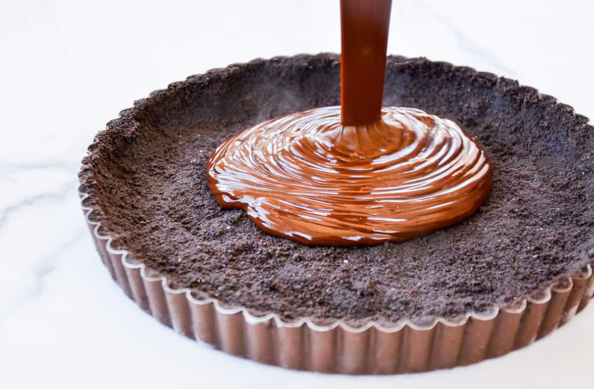 Chocolate ganache being poured into an Oreo cookie tart crust.