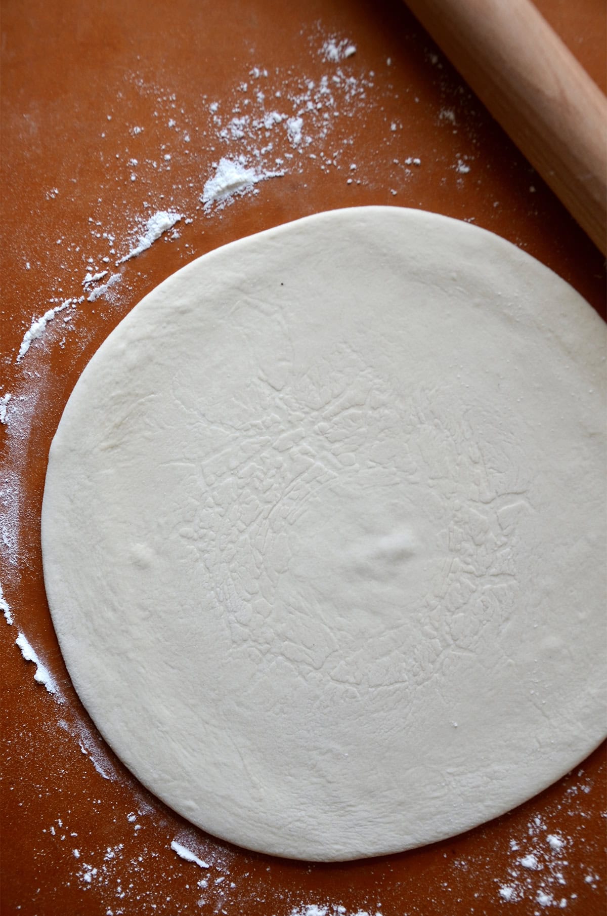 A round of pizza dough on a floured surface with a rolling pin beside it.