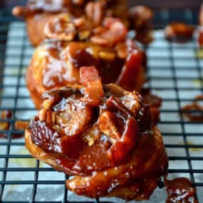 Sticky buns topped with bacon and pecans on a wire cooling rack.
