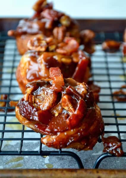 Sticky buns topped with bacon and pecans on a wire cooling rack.