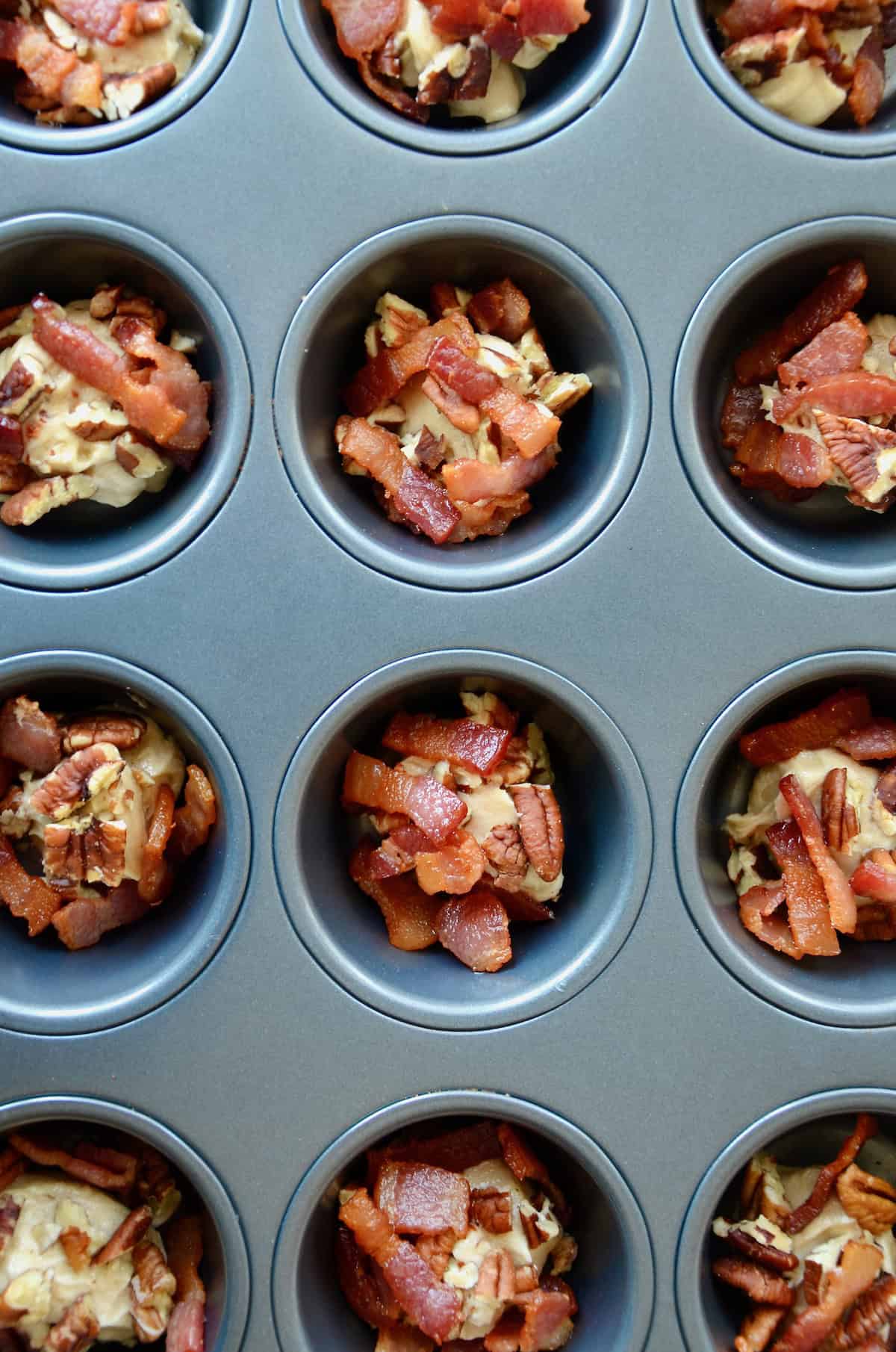 Butter and chopped bacon and pecans in the wells of a muffin tin.