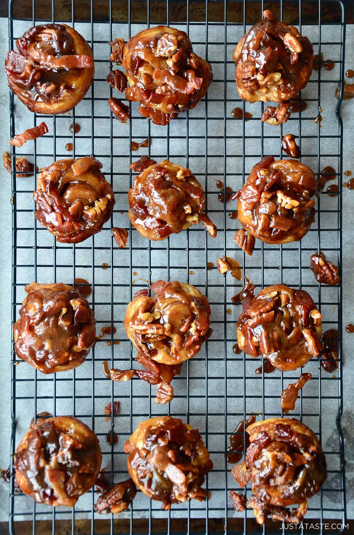 Sticky buns topped with chopped bacon and pecans on a wire cooling rack.