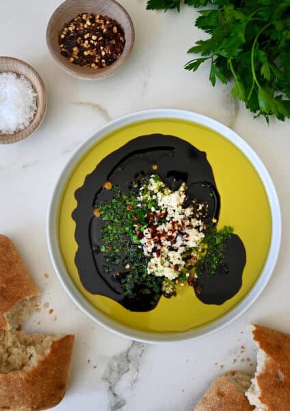 The best bread dipping oil in a shallow plate next to chunks of crusty bread.