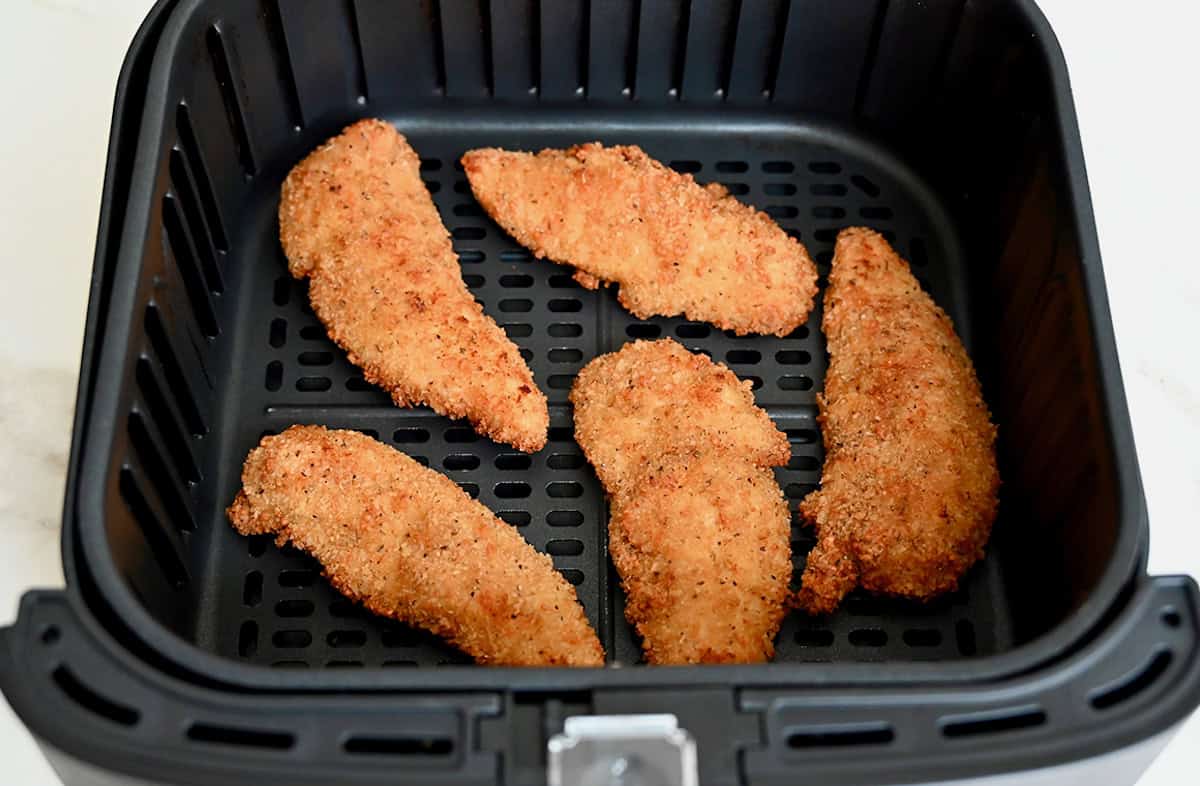 Crispy chicken tenders in the basket of an air fryer.