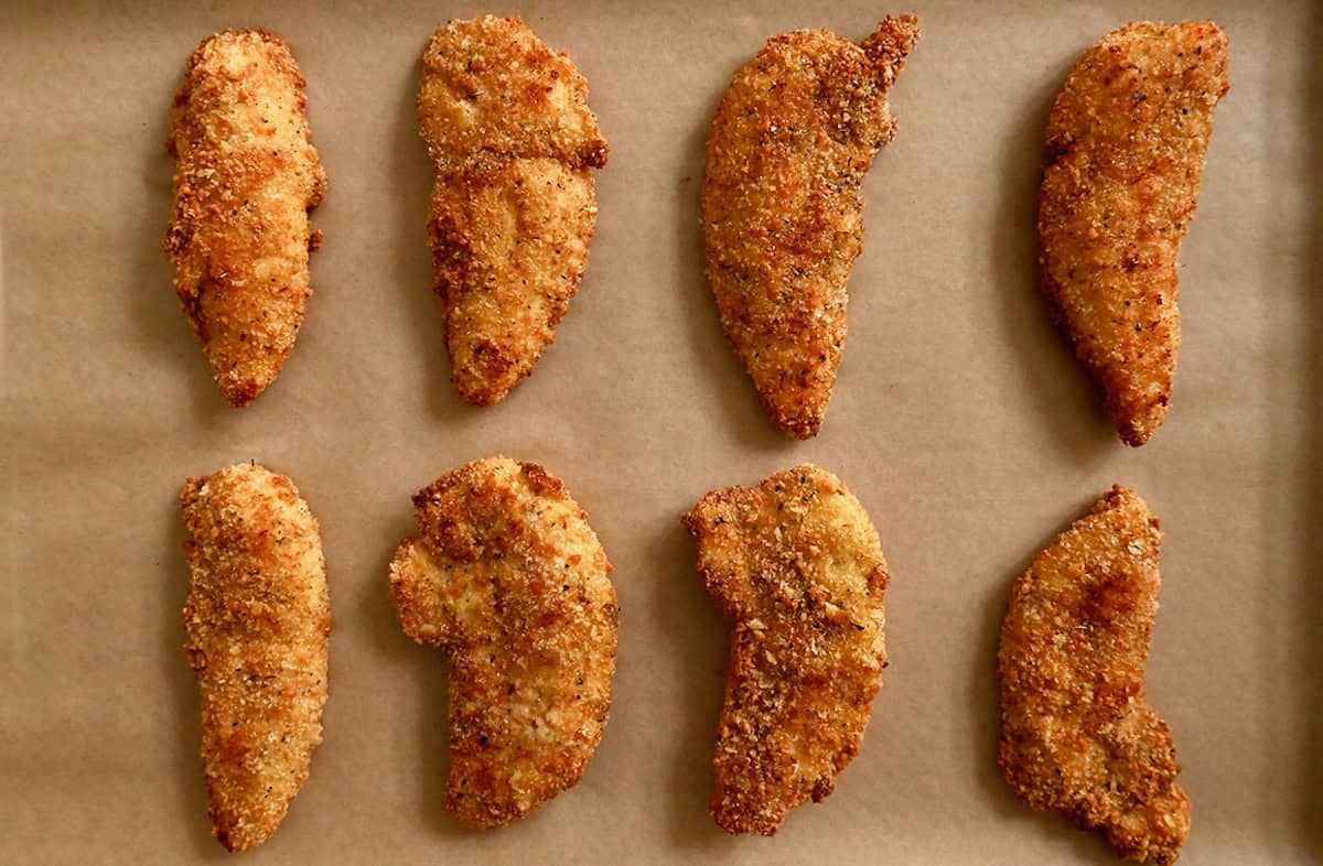 Crispy chicken tenders on a parchment-lined baking sheet.