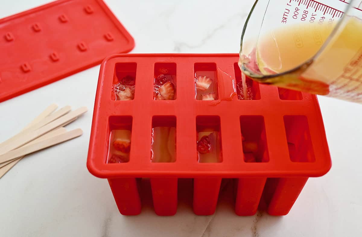 A person using a measuring cup to fill a popsicle mold with peach sangria popsicle mix.