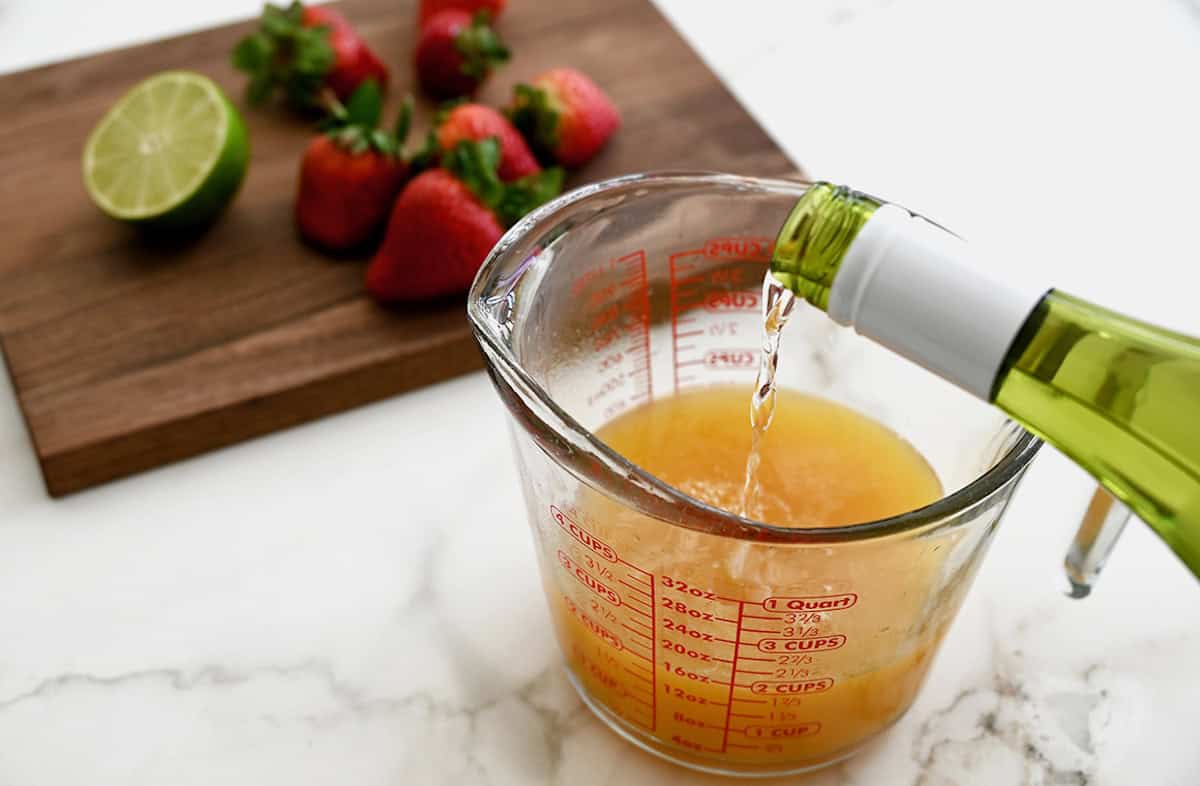 White wine being poured into a measuring cup containing peach juice.