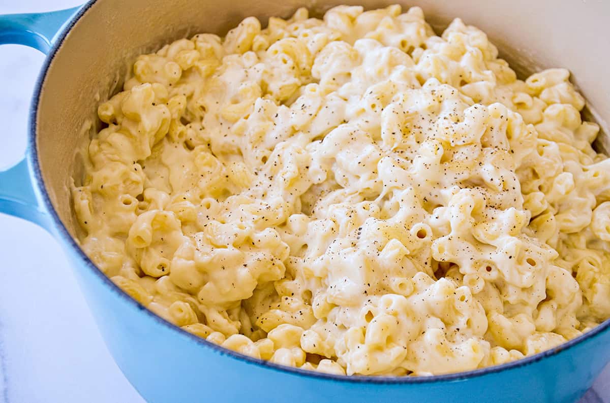 A blue Dutch oven is filled with white cheddar mac and cheese seasoned with black pepper.