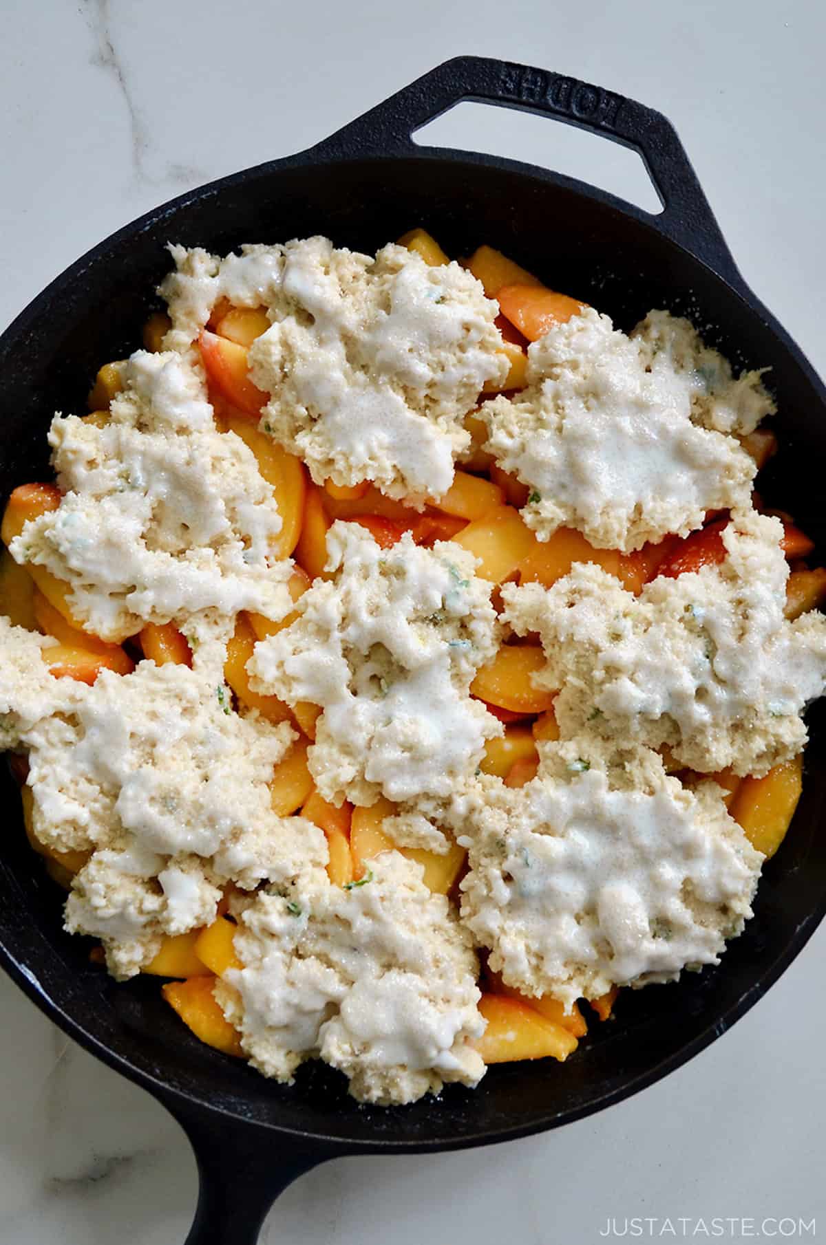 Peaches in a cast iron skillet are topped with raw biscuit dough flecked with thyme and brushed with buttermilk.