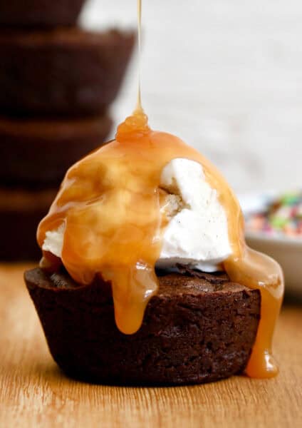 A fudge brownie cupcake topped with vanilla ice cream and a drizzle of caramel sauce.