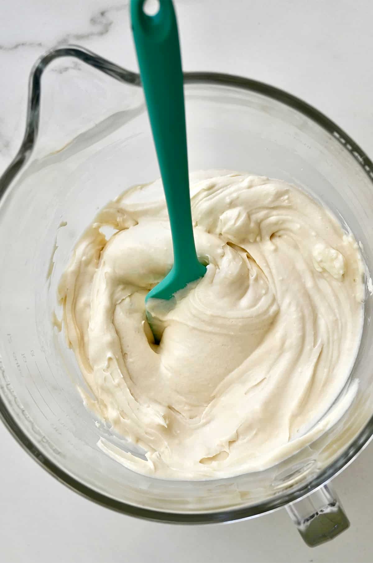 Smooth cream cheese frosting in a bowl with a spatula.