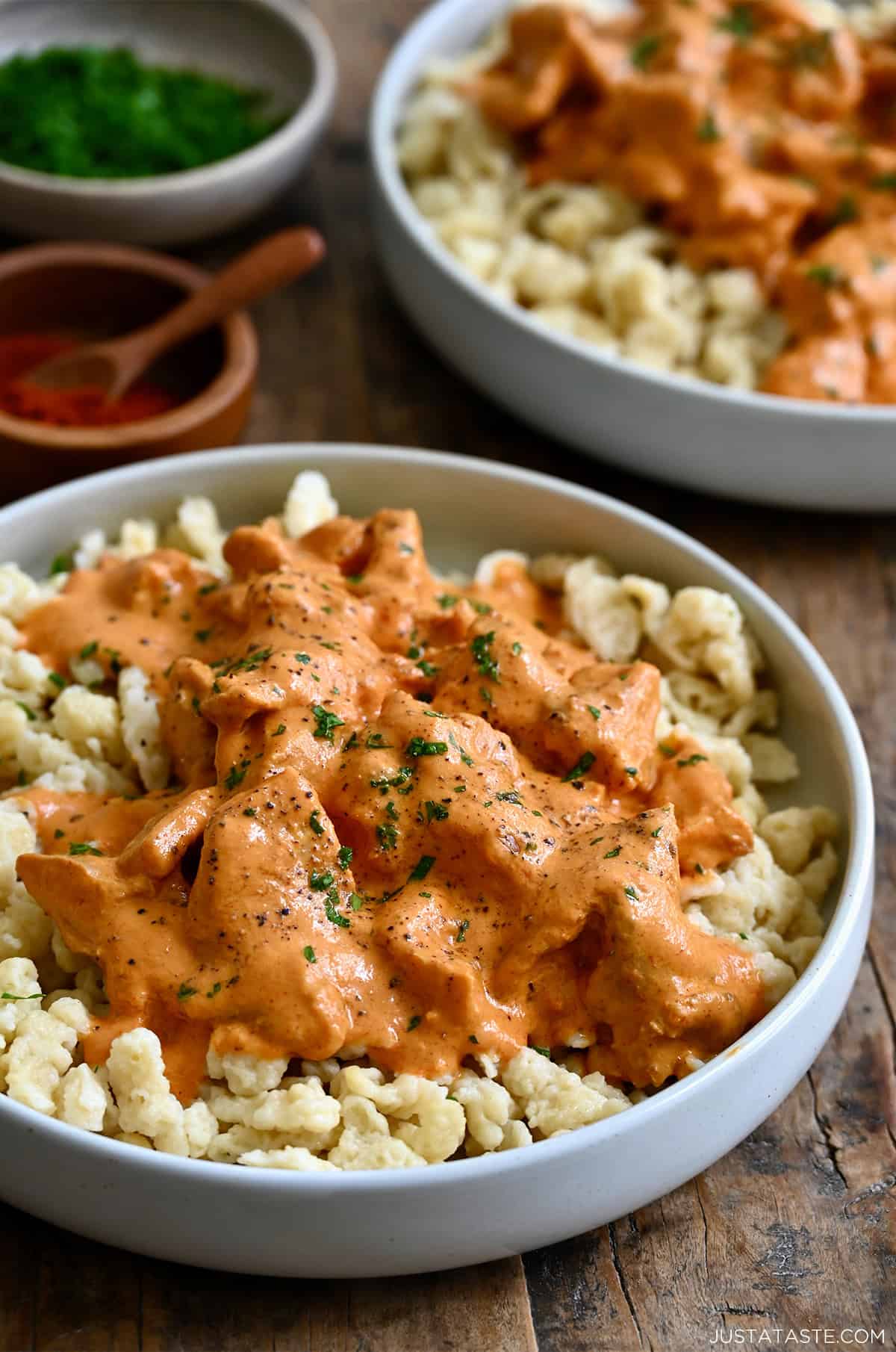 Chicken paprikas atop spaetzle on a white dinner plate.