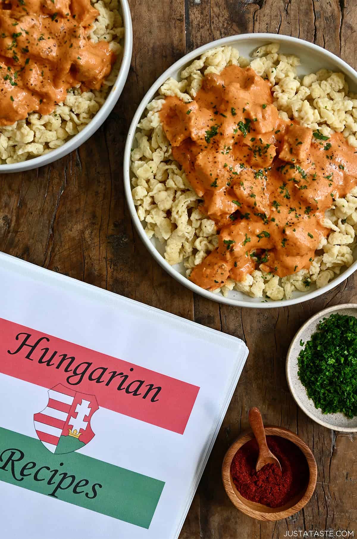 Hungarian recipes binder next to two dinner plates with Hungarian chicken paprikash atop nokedli.