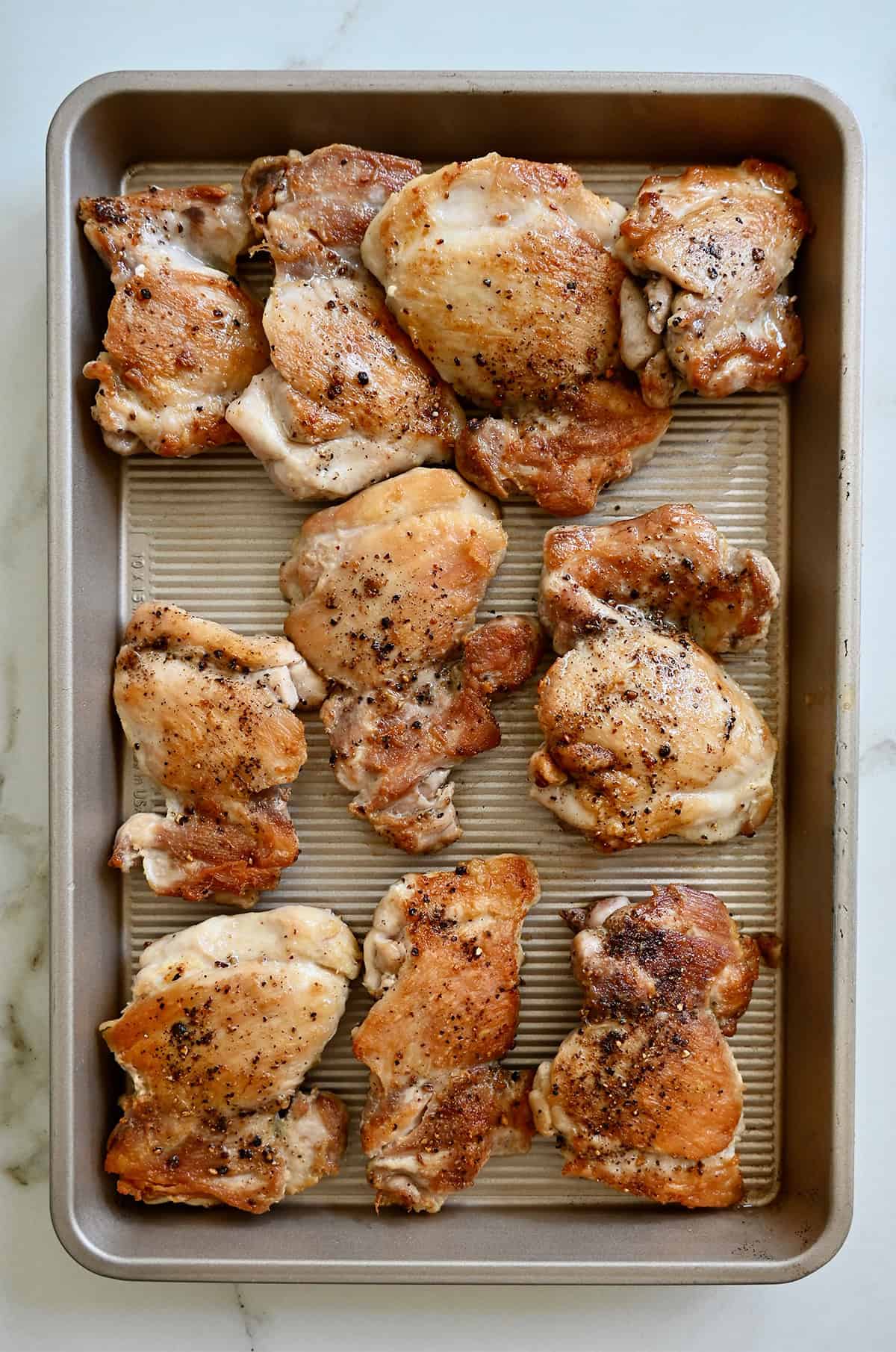 Browned chicken thighs on a baking sheet.