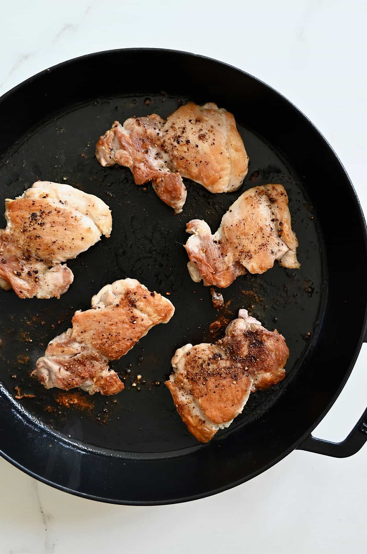 Seared chicken thighs in a pan.