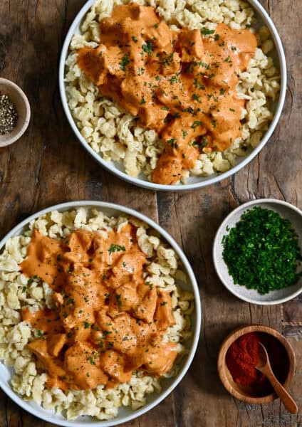 Two plates containing Hungarian chicken paprikas over nokedli.