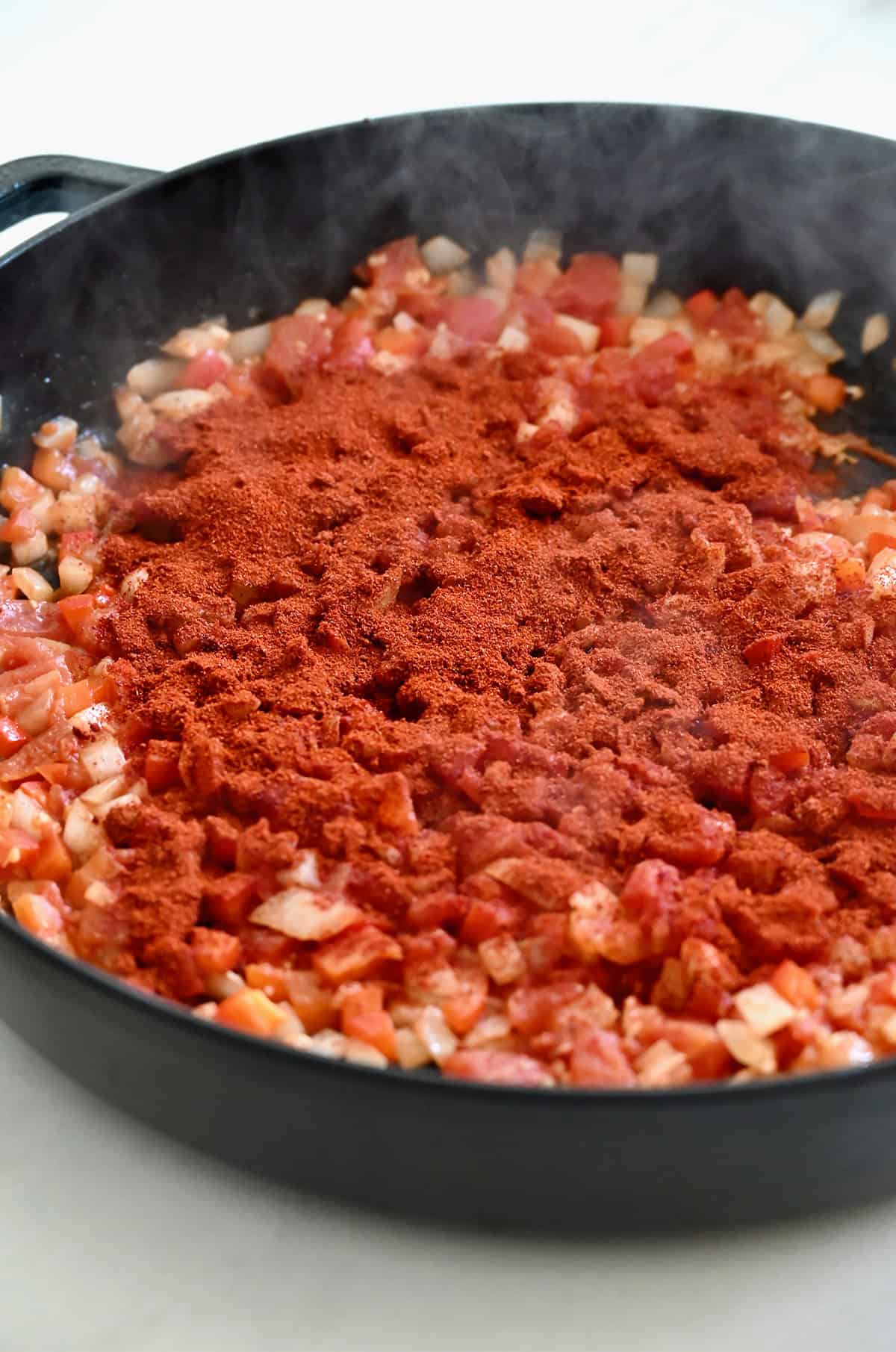 Hungarian paprika atop cooked diced veggies in a large skillet.