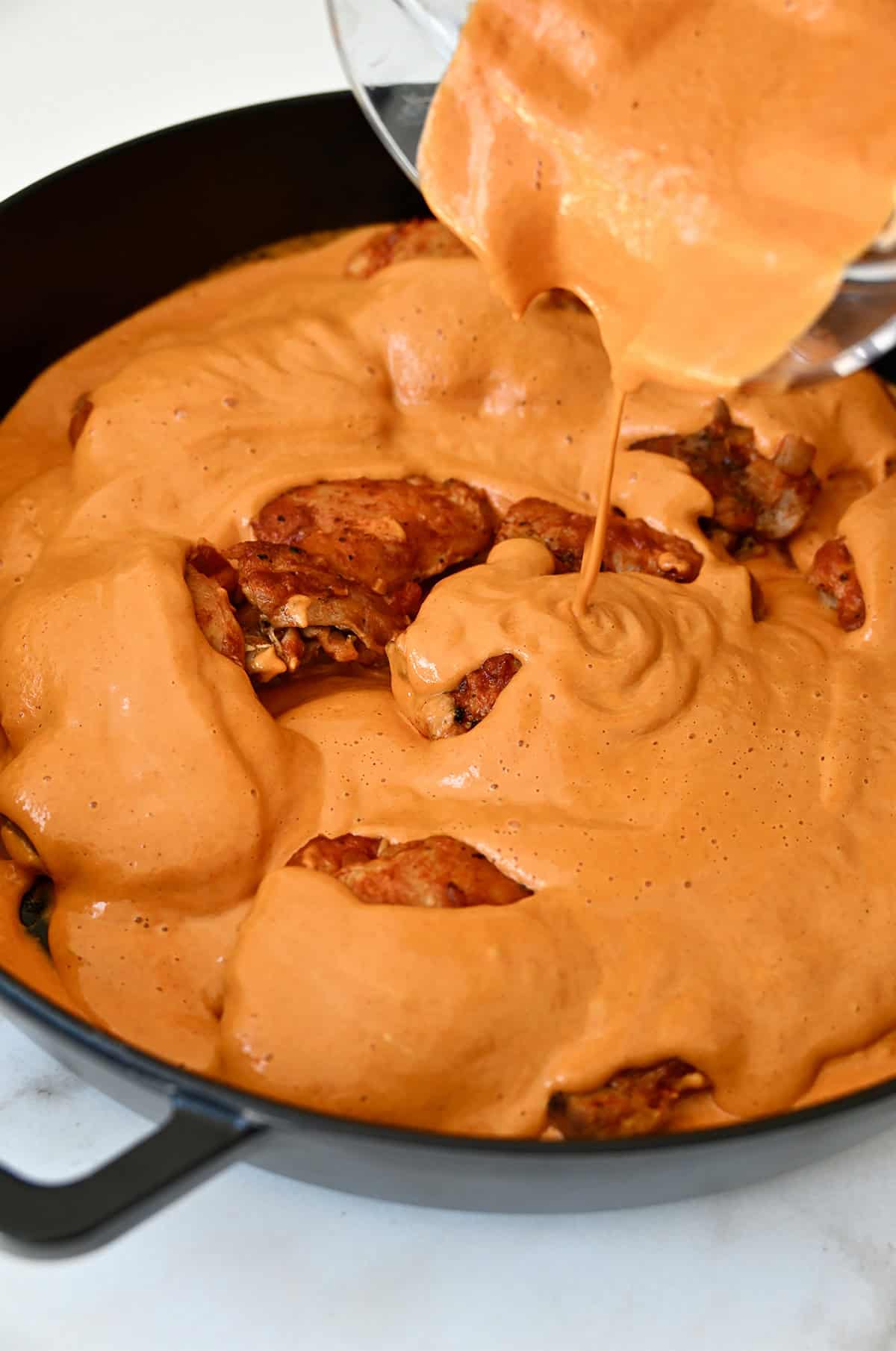 Creamy paprika sauce being poured over braised chicken thighs in a skillet.