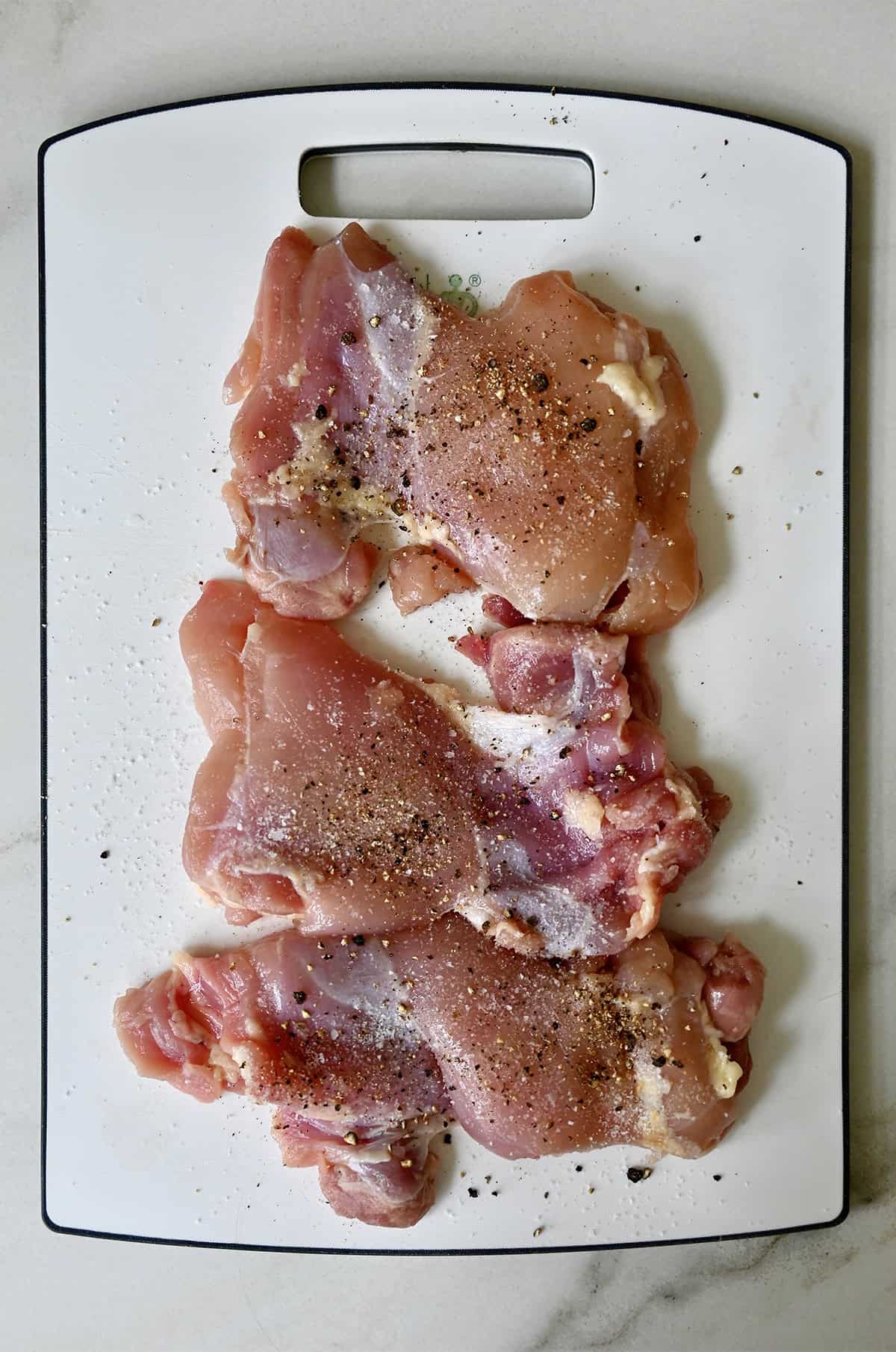 Chicken thighs generously seasoned with salt and pepper.