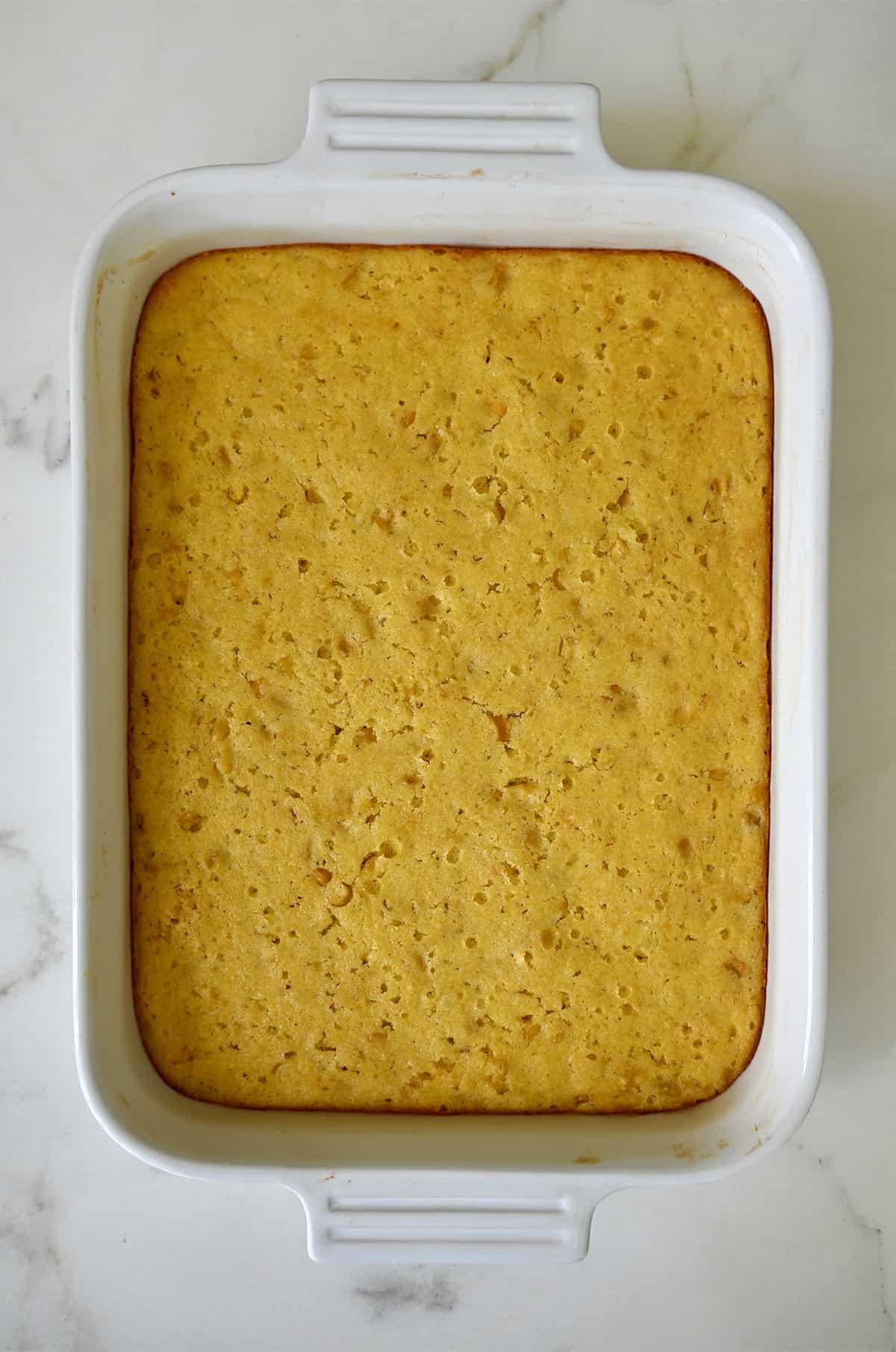 Freshly baked cornbread casserole in a white baking dish.