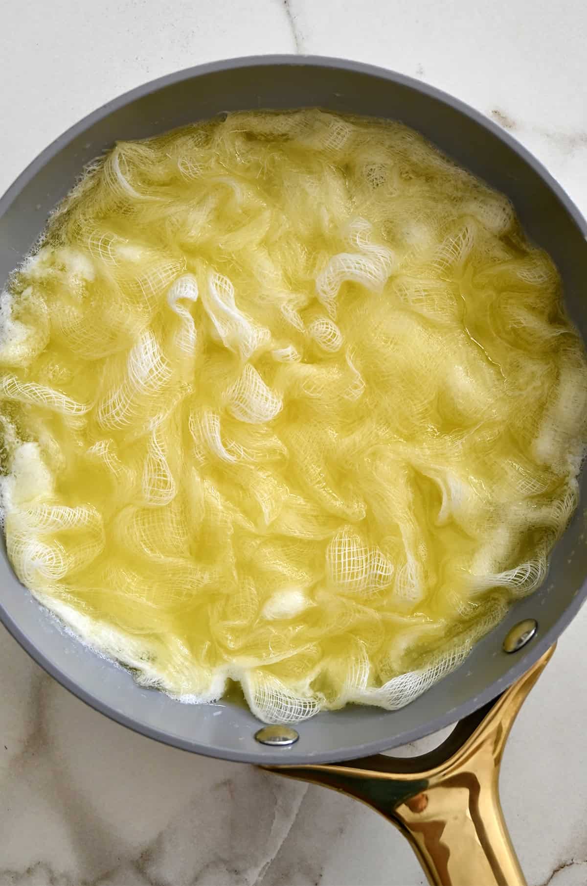 A cheesecloth soaking up melted butter in a large skillet.