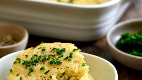 A scoop of corn casserole topped with fresh chives and melted butter in a small bowl.