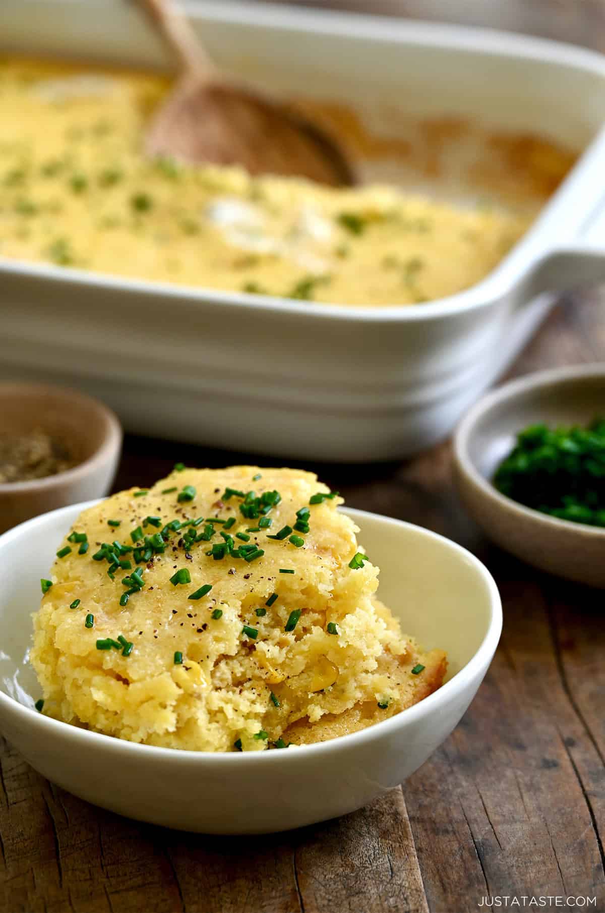 A scoop of corn casserole topped with fresh chives and melted butter in a small bowl.