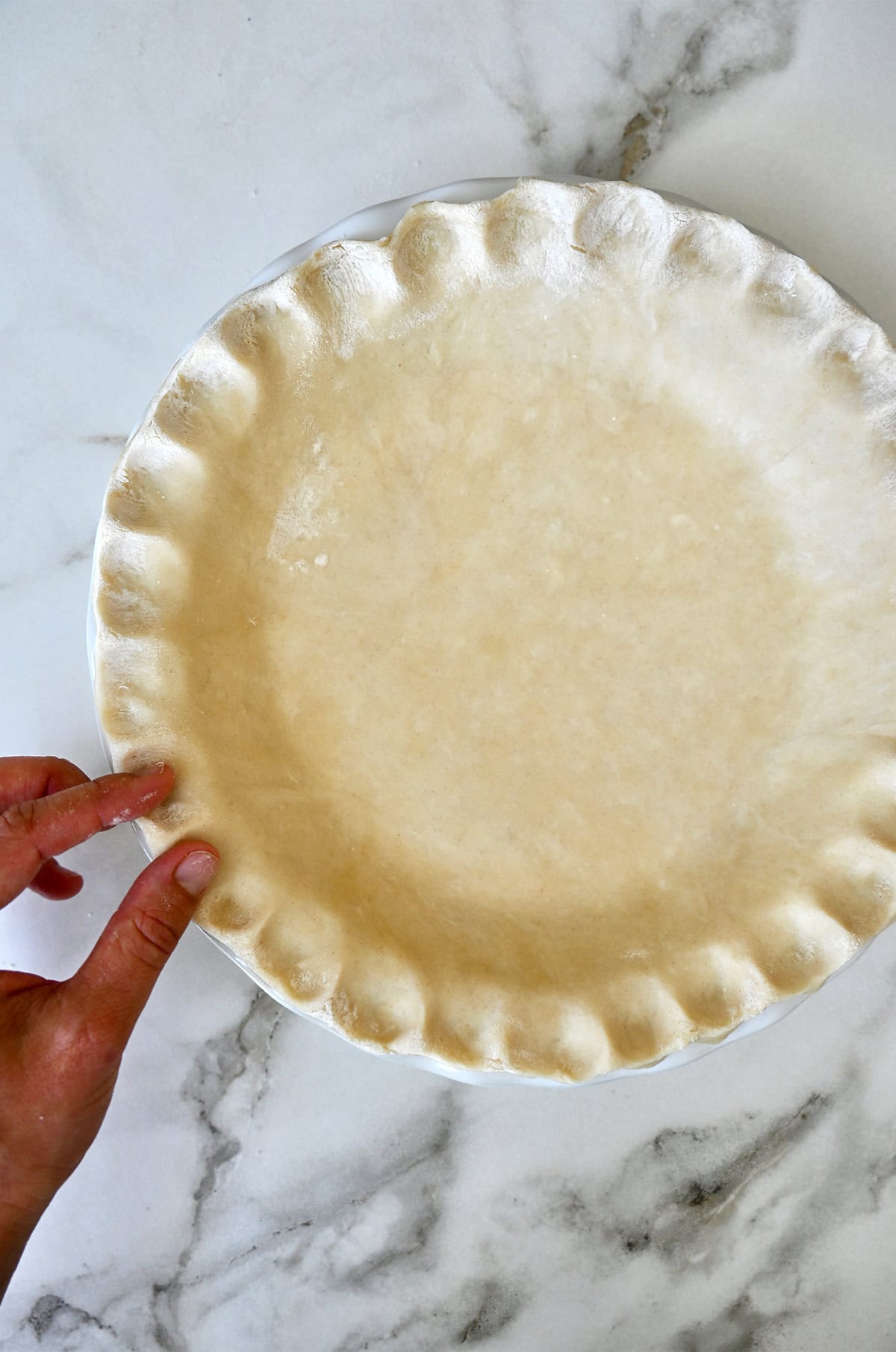 Fluting the pie crust with fingers for that classic, scalloped look.
