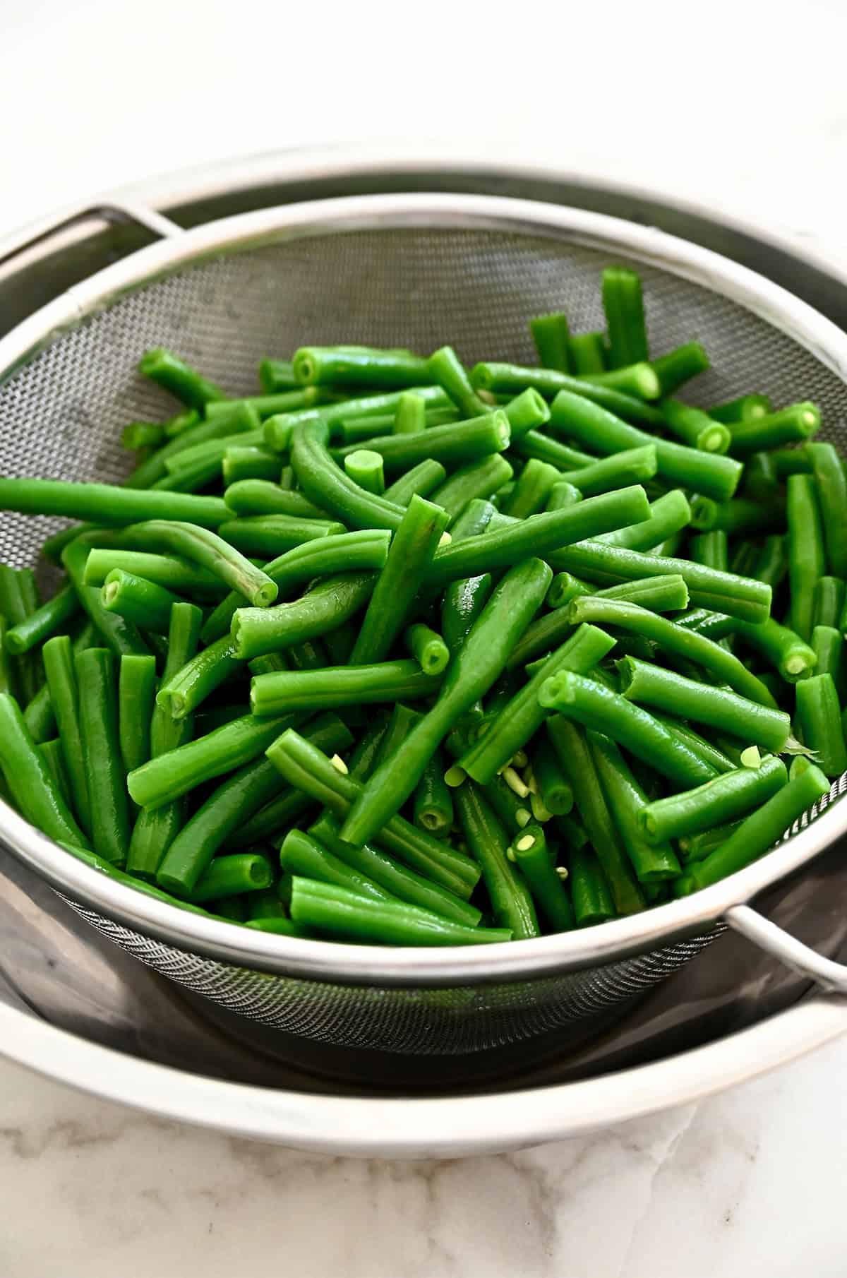 Blanched green beans draining in a sieve over a bowl.