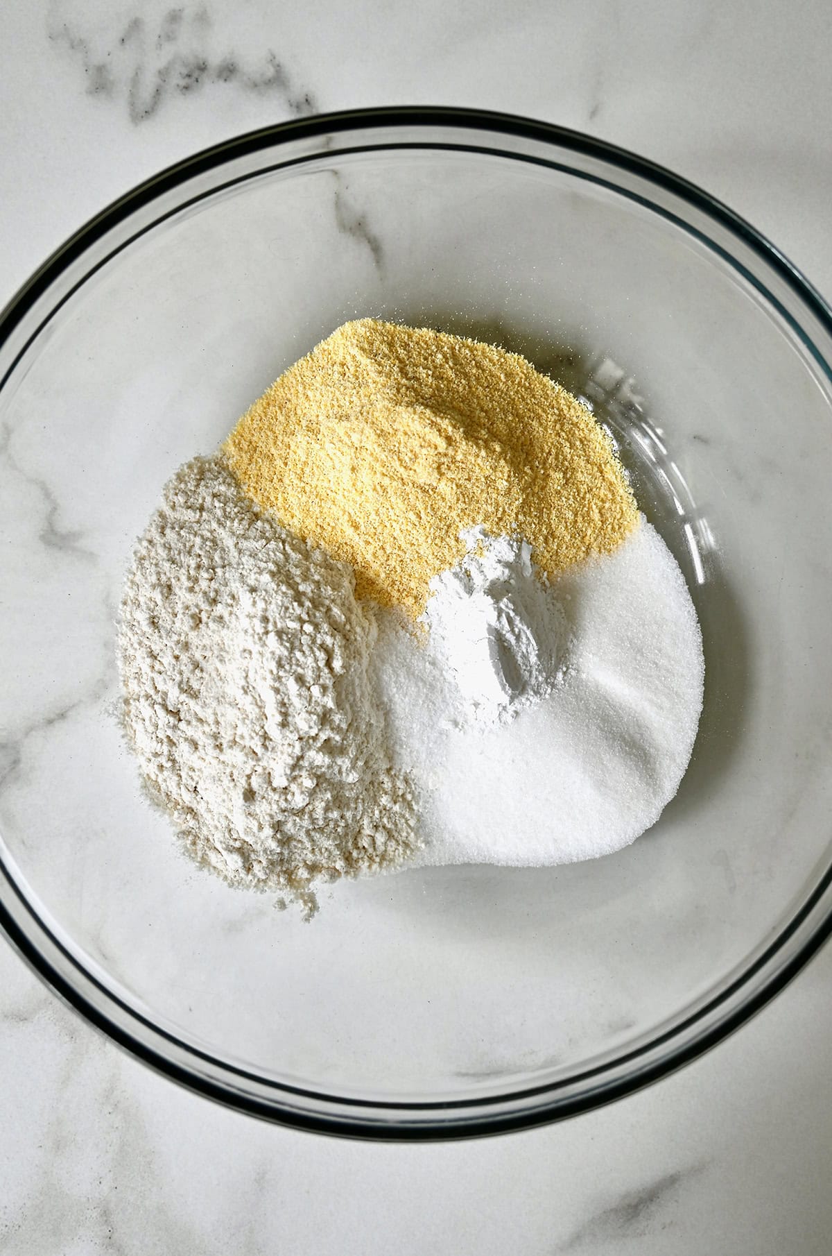 Yellow cornmeal, flour, baking powder, sugar and salt in a glass bowl.