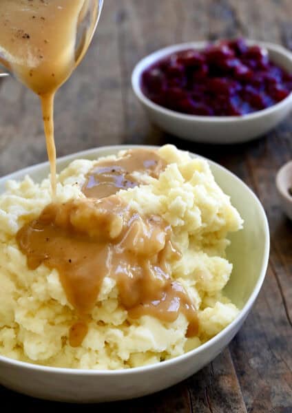 Homemade gravy being poured over mashed potatoes in a large serving bowl.