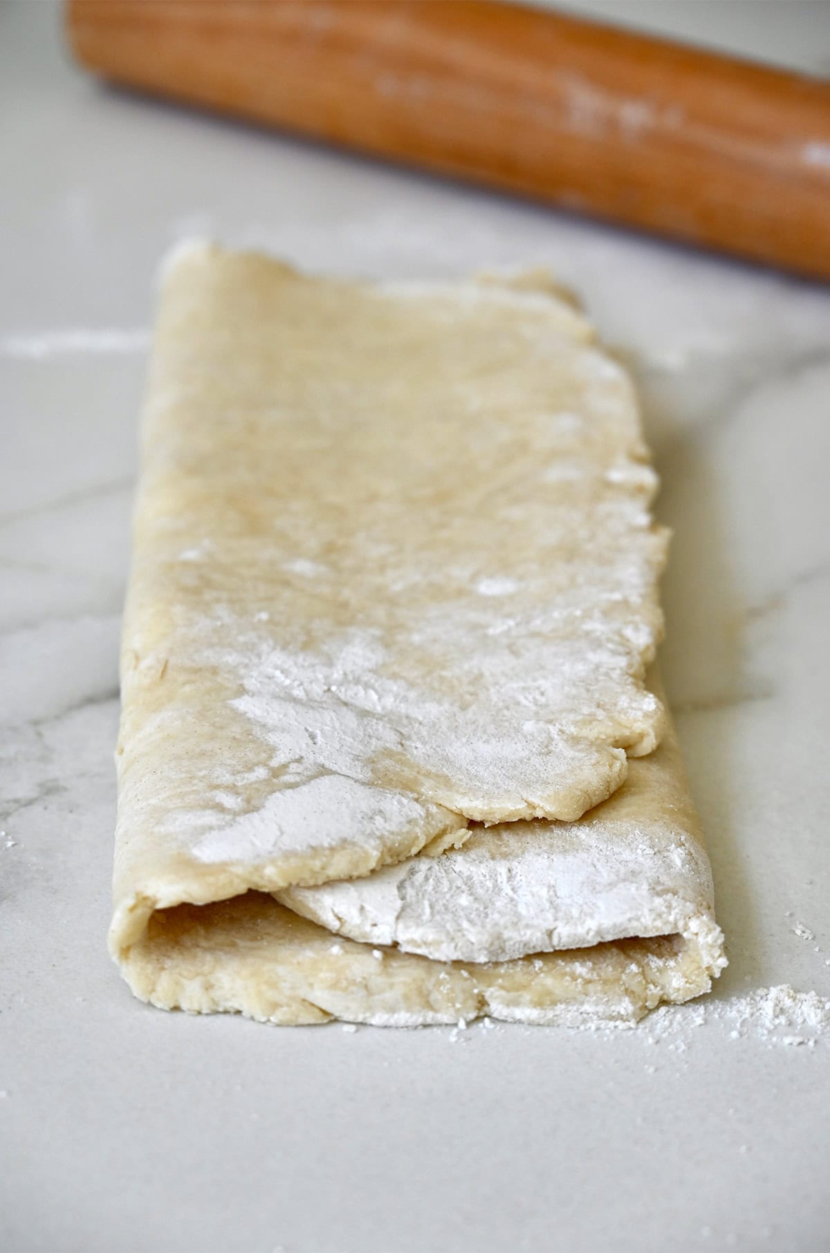 Folded pie dough on a floured marble surface.
