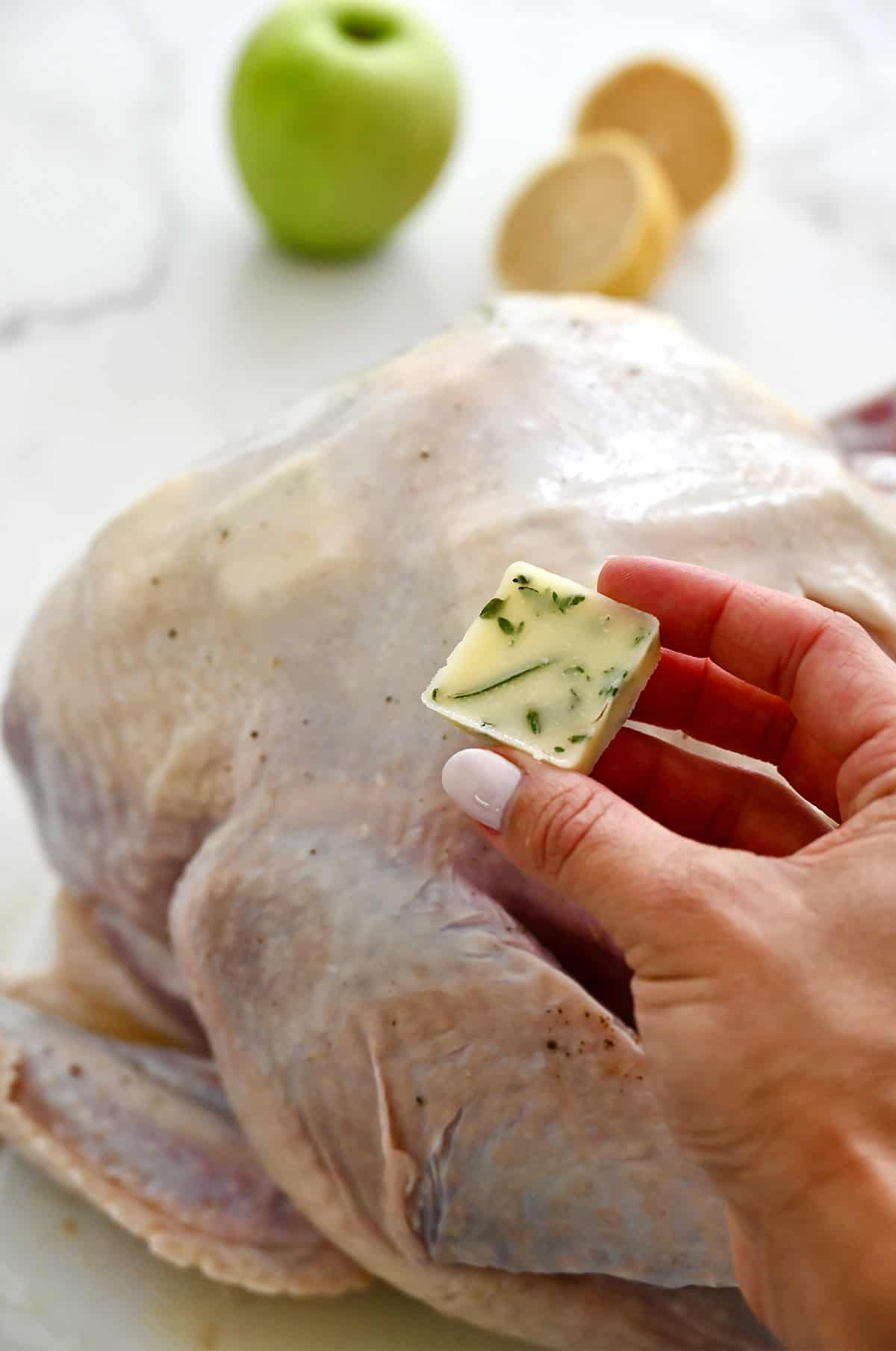 Frozen butter cubes being placed underneath the skin of an uncooked turkey.