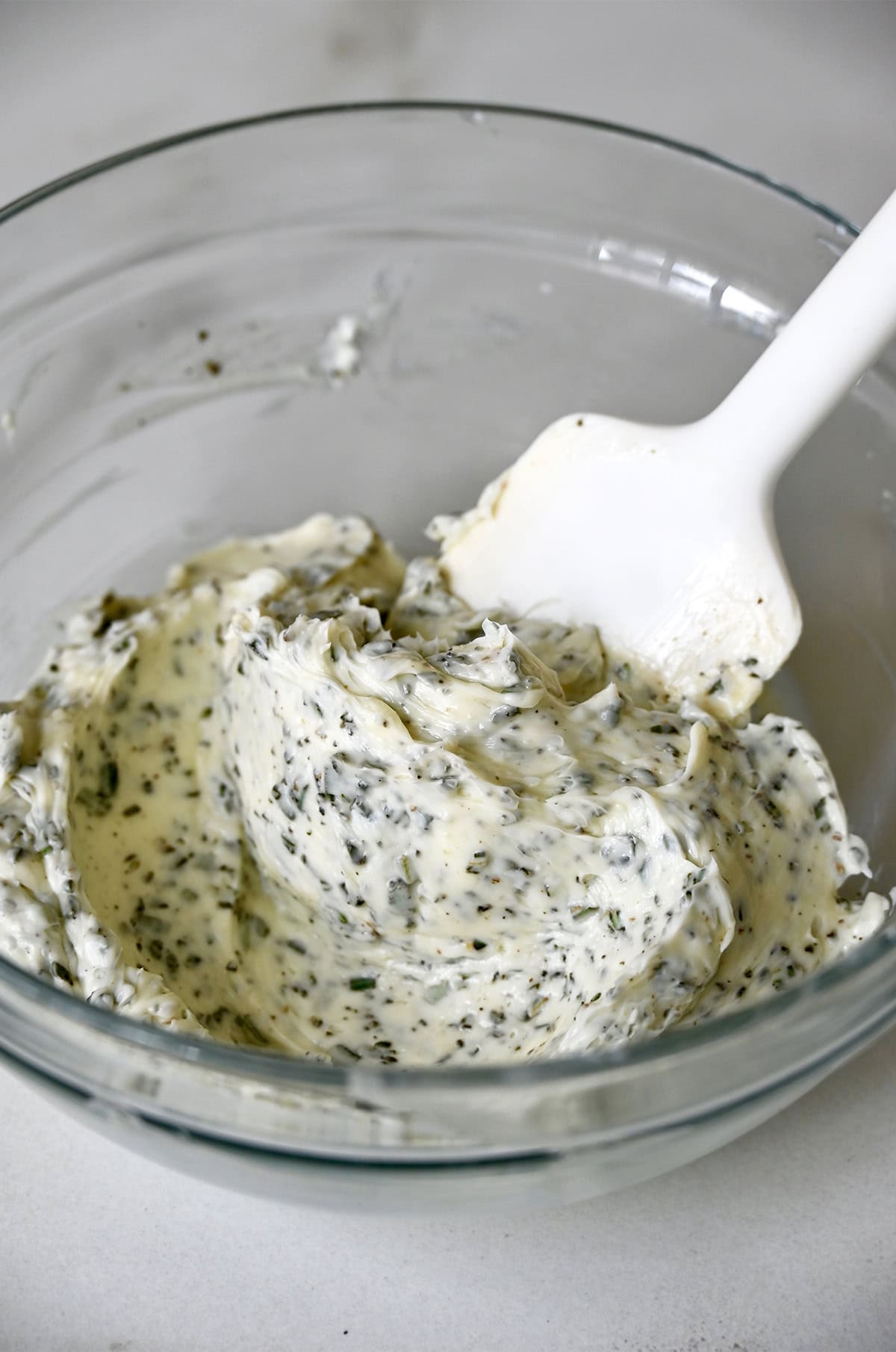 Herb butter in a glass bowl with a spatula.