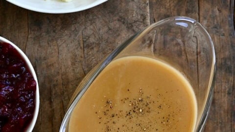 Homemade gravy in a gravy boat next to a bowl with cranberry sauce and a bowl of mashed potatoes.