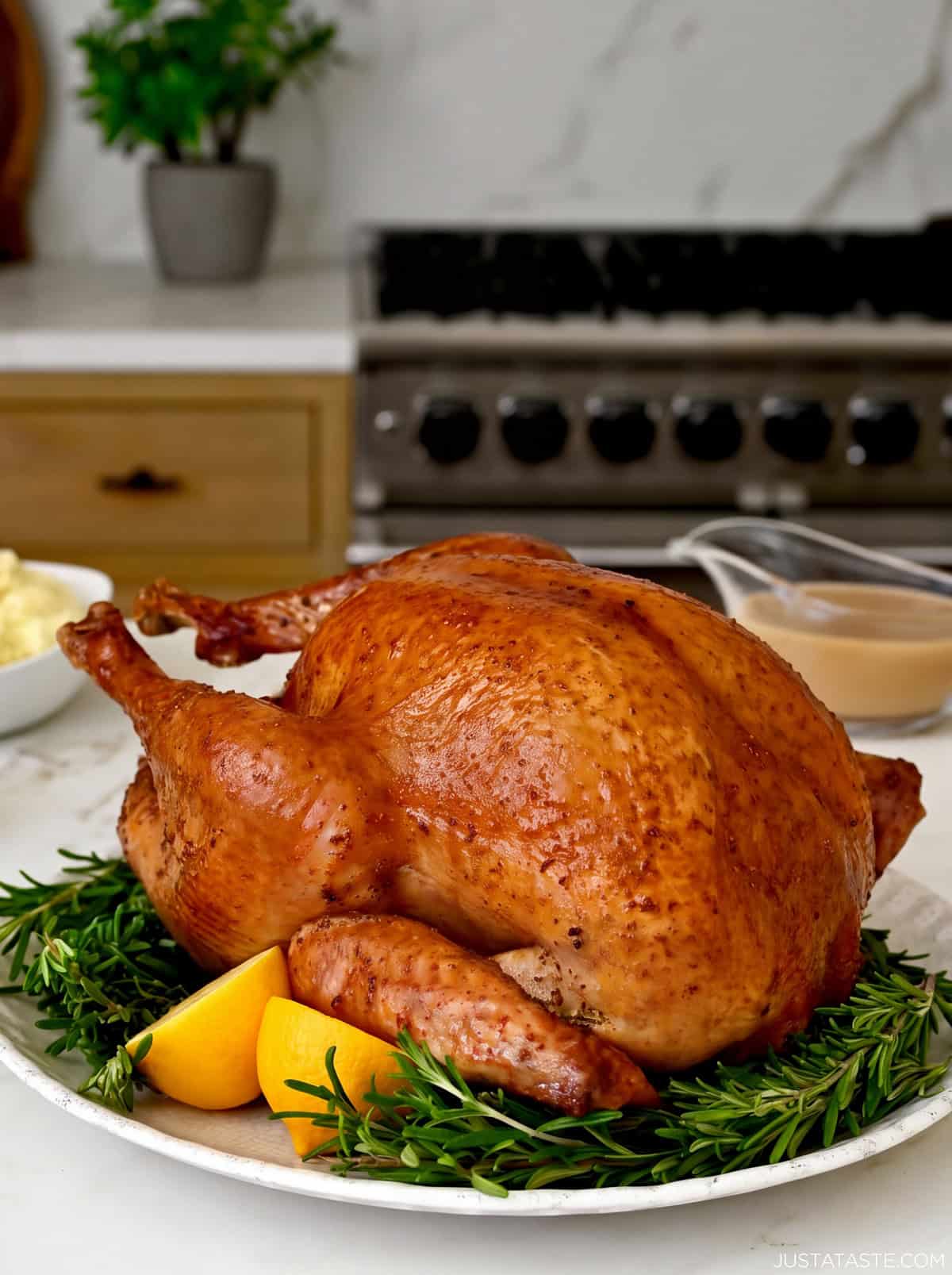 Juicy roasted Thanksgiving turkey on a serving platter with fresh thyme and a lemon cut in half. A gravy bowl is nearby.