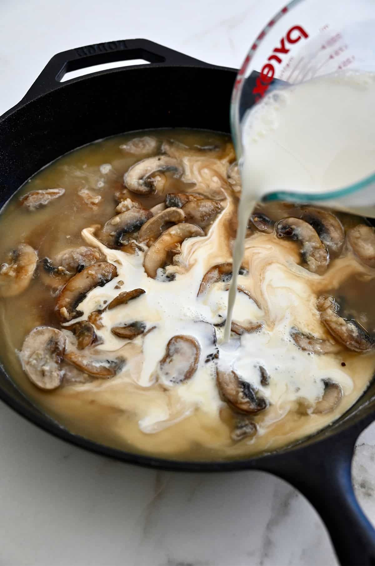 Half-and-half being added to a skillet with sautéed mushrooms to make mushroom sauce.