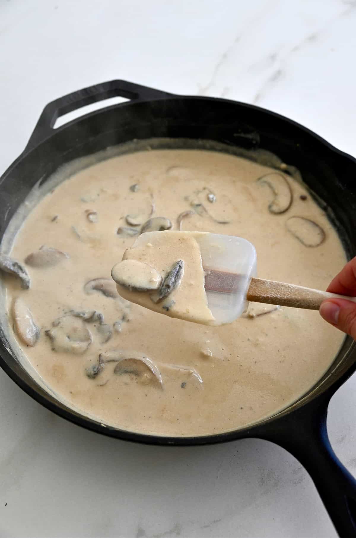 Homemade cream of mushroom soup in a skillet and coating a spatula.