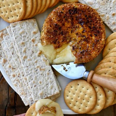 Gooey pan-fried brie with pistachios and honey on a plate surrounded by crackers.