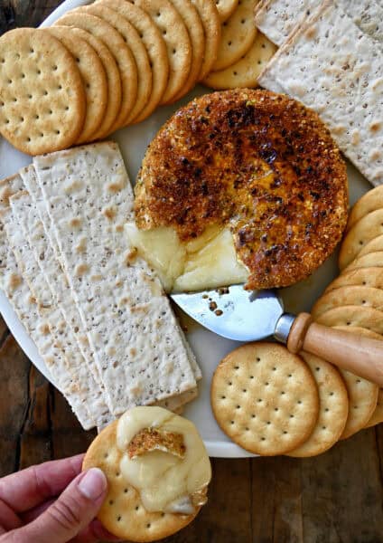 Gooey pan-fried brie with pistachios and honey on a plate surrounded by crackers.