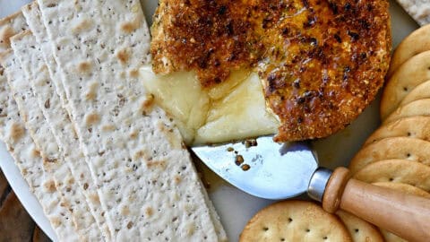 Gooey pan-fried brie with pistachios and honey on a plate surrounded by crackers.