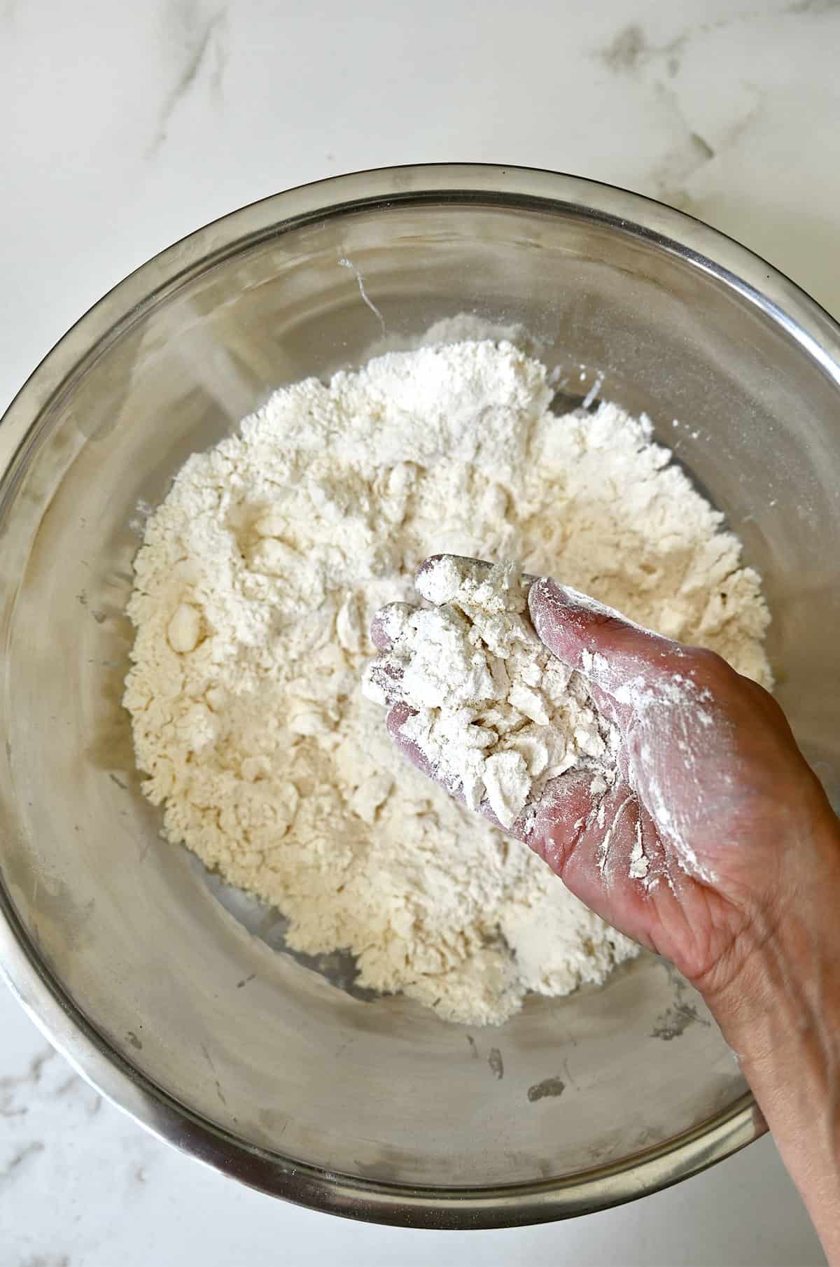 A bowl containing a flour mixture with cold, cubed butter the consistency of wet sand.